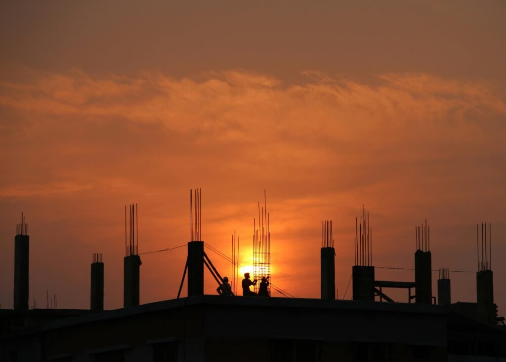 zipwp-image-176342 Silhouette of workers on a construction site against a vibrant sunset sky.